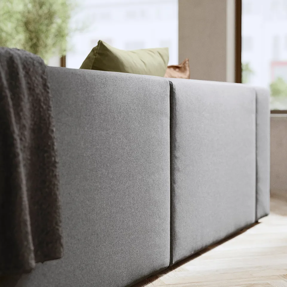 Modern grey modular sofa with green pillow, atop wooden floor.