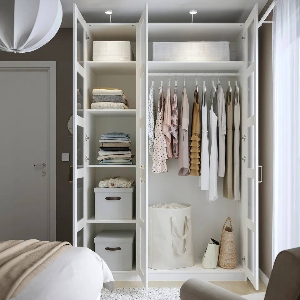 Open white PAX wardrobe displaying neatly folded clothes, hanging garments, grey storage boxes, and a laundry bag on shelves and hanging rod.
