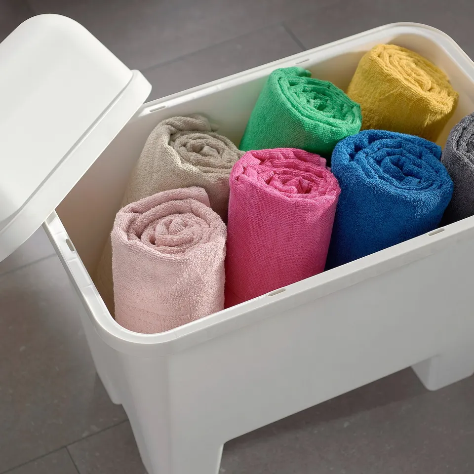 White plastic storage bin, lid open, holding neatly rolled towels of different colours.