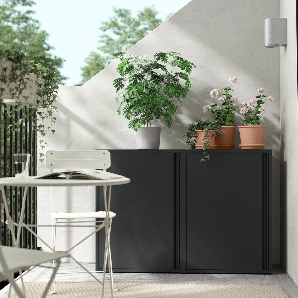 Modern balcony setup with SUNDSÖ black cabinet, white chairs, and potted plants.