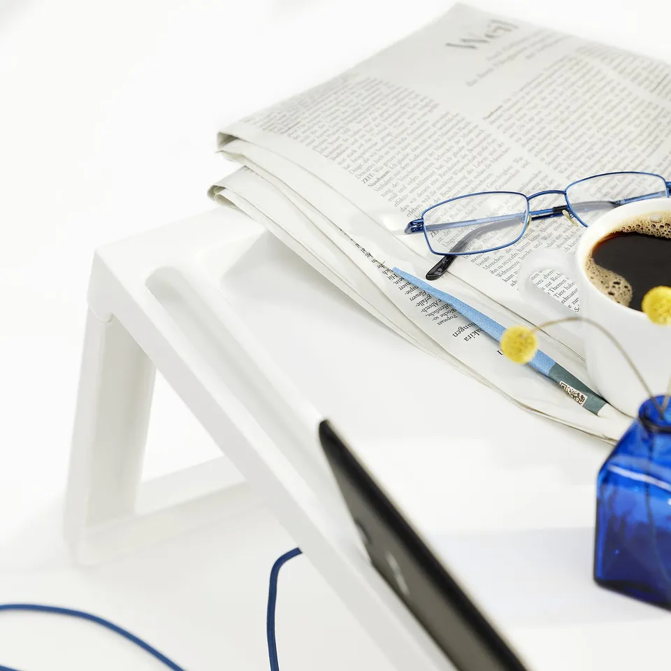 Newspapers, glasses, and coffee cup on KLIPSK tray with secure groove and charging hole.
