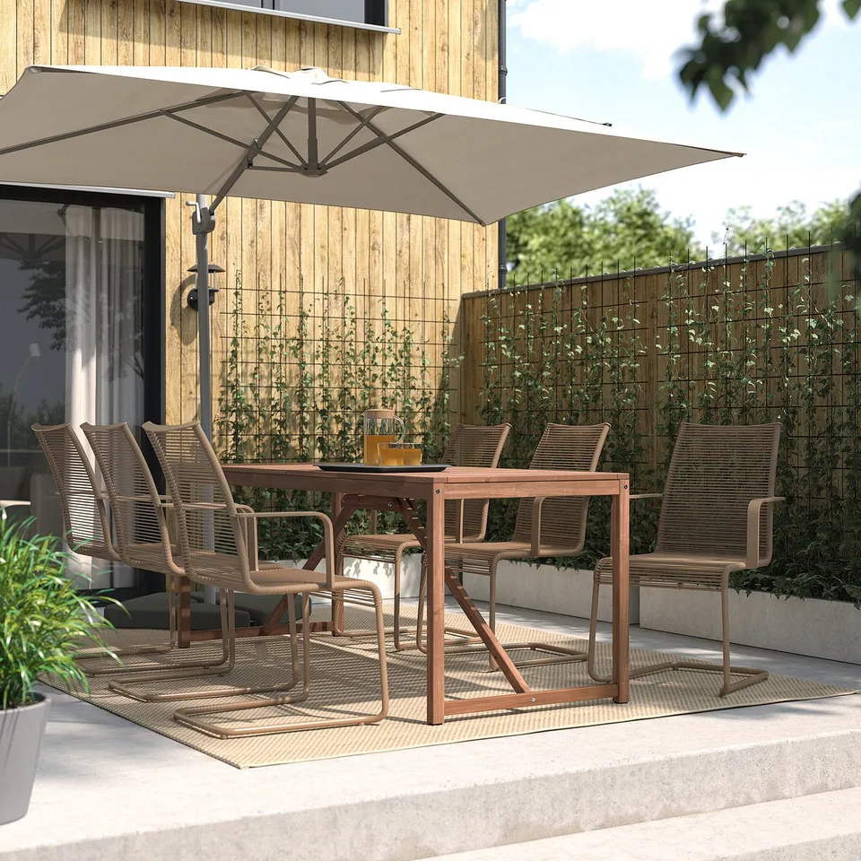 Outdoor dining setup with VÄSMAN brown chairs & table, white umbrella, plants, on a rug.