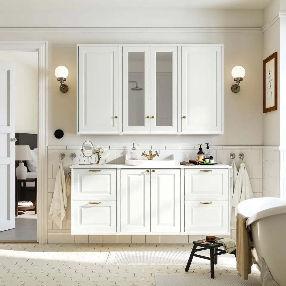 Modern bathroom with FRIHULT lights, gold-handled cabinet, black stool by tub, cream walls, and herringbone floor.