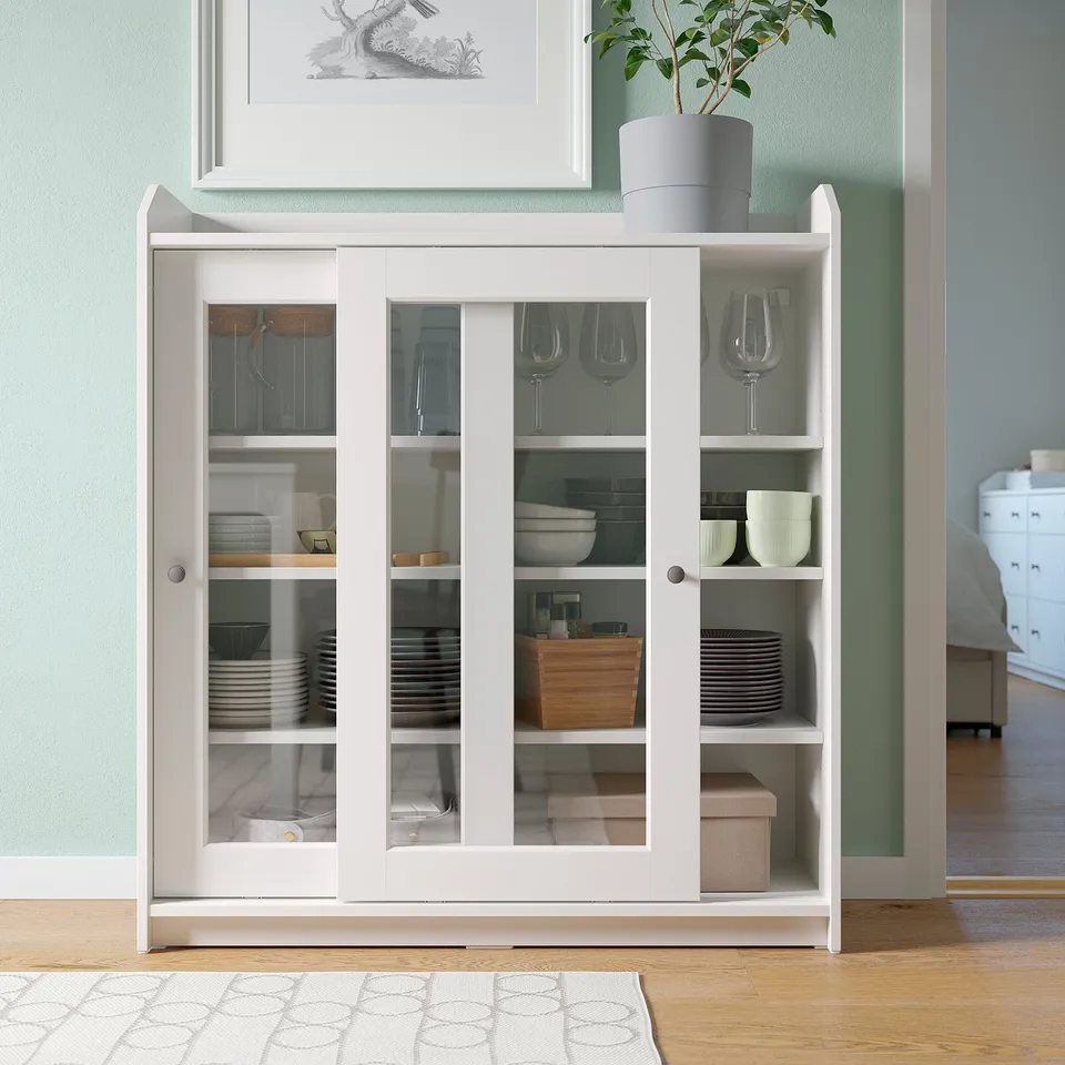 White HAUGA storage cabinet with glass doors. Holds dishes, glasses, and decor. Modern design, wooden and glass material.