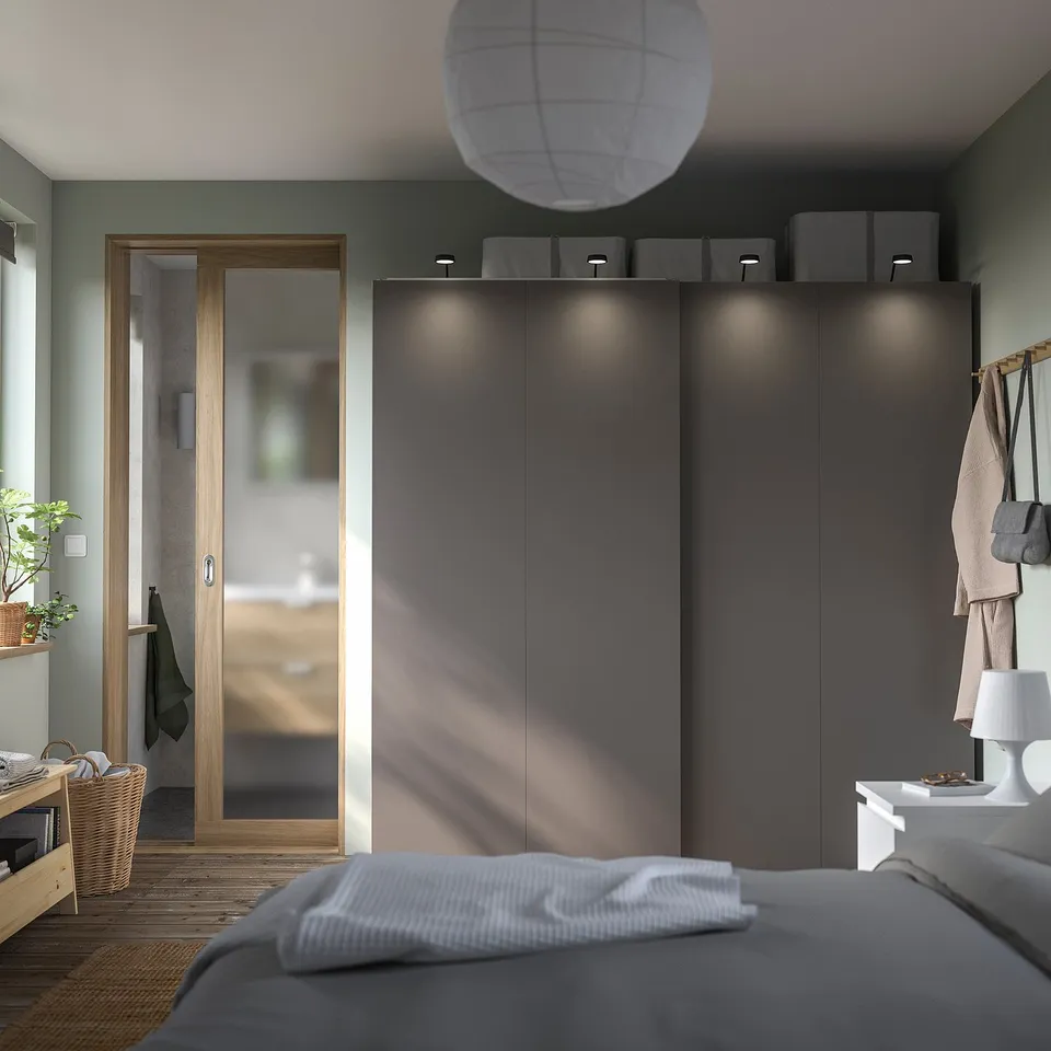 Modern bedroom with grey HASVIK sliding closet doors, grey bed, white lamp, and a wooden door leading outside.