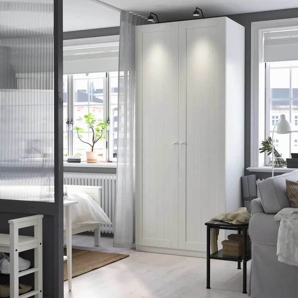 Modern bedroom with large white PAX wardrobe, grey curtains, bed, and armchair, highlighting room layout and decor.