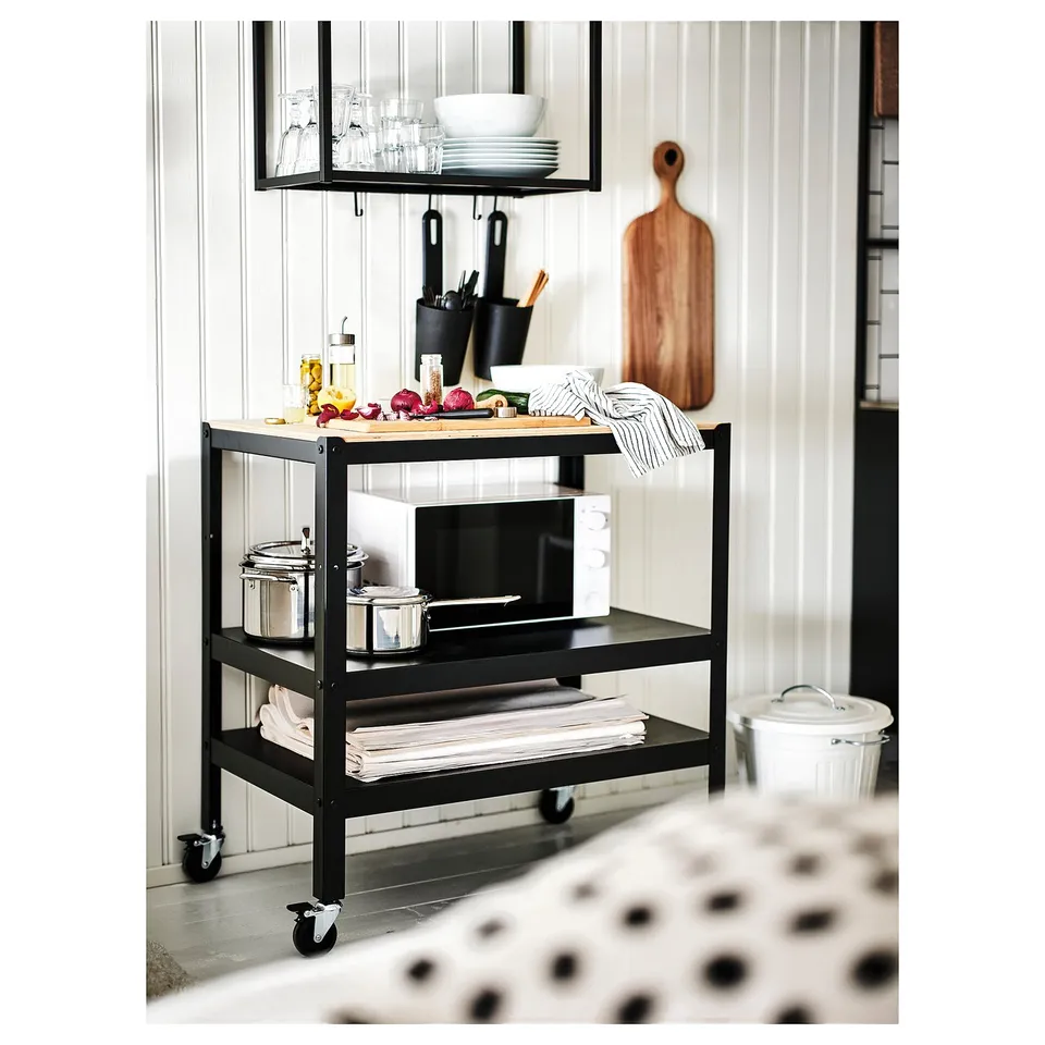 Black BROR kitchen cart with wooden top, holding microwave, canisters, and fresh produce. Open shelving design with locked castors for stability.