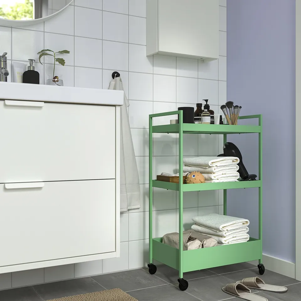 Modern bathroom with white cabinet & green NISSAFORS trolley. Trolley holds towels, toiletries & cosmetics. Small, mobile, metallic, 3-tiered.