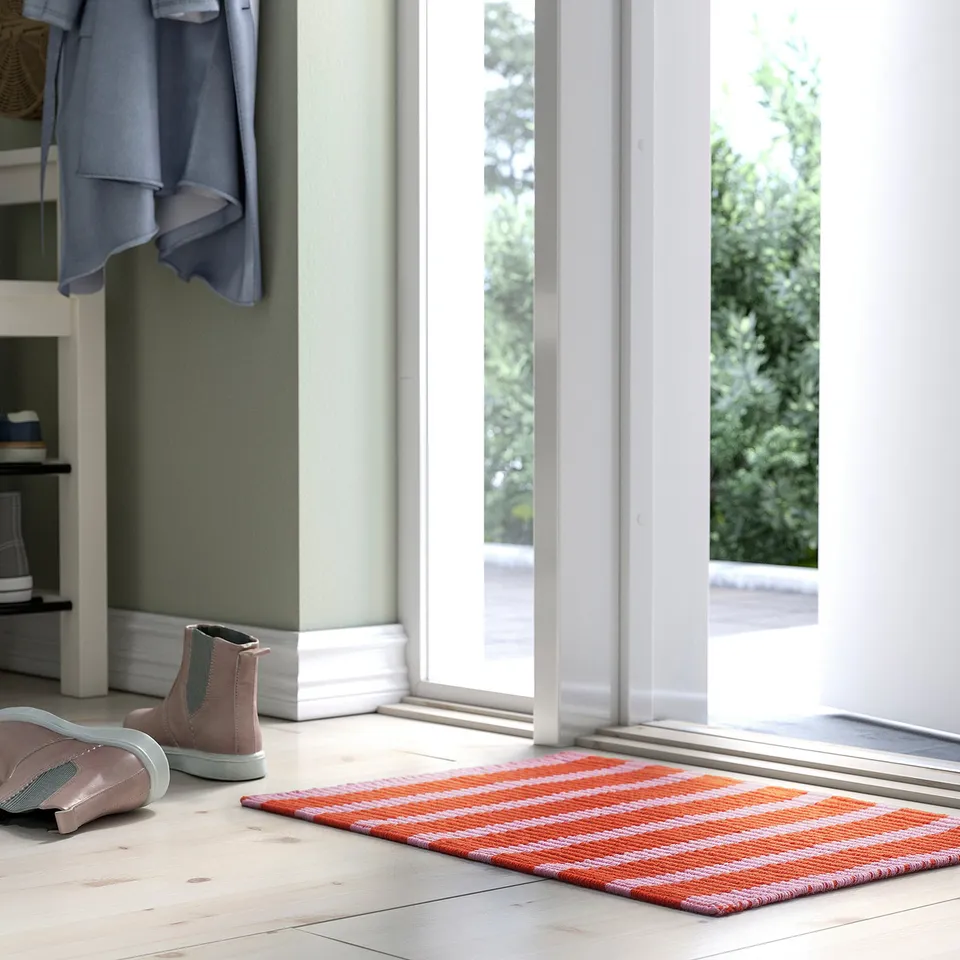 Orange and white striped VÄGSKYLT mat near glass door, fits entrance, cotton with grip backing.