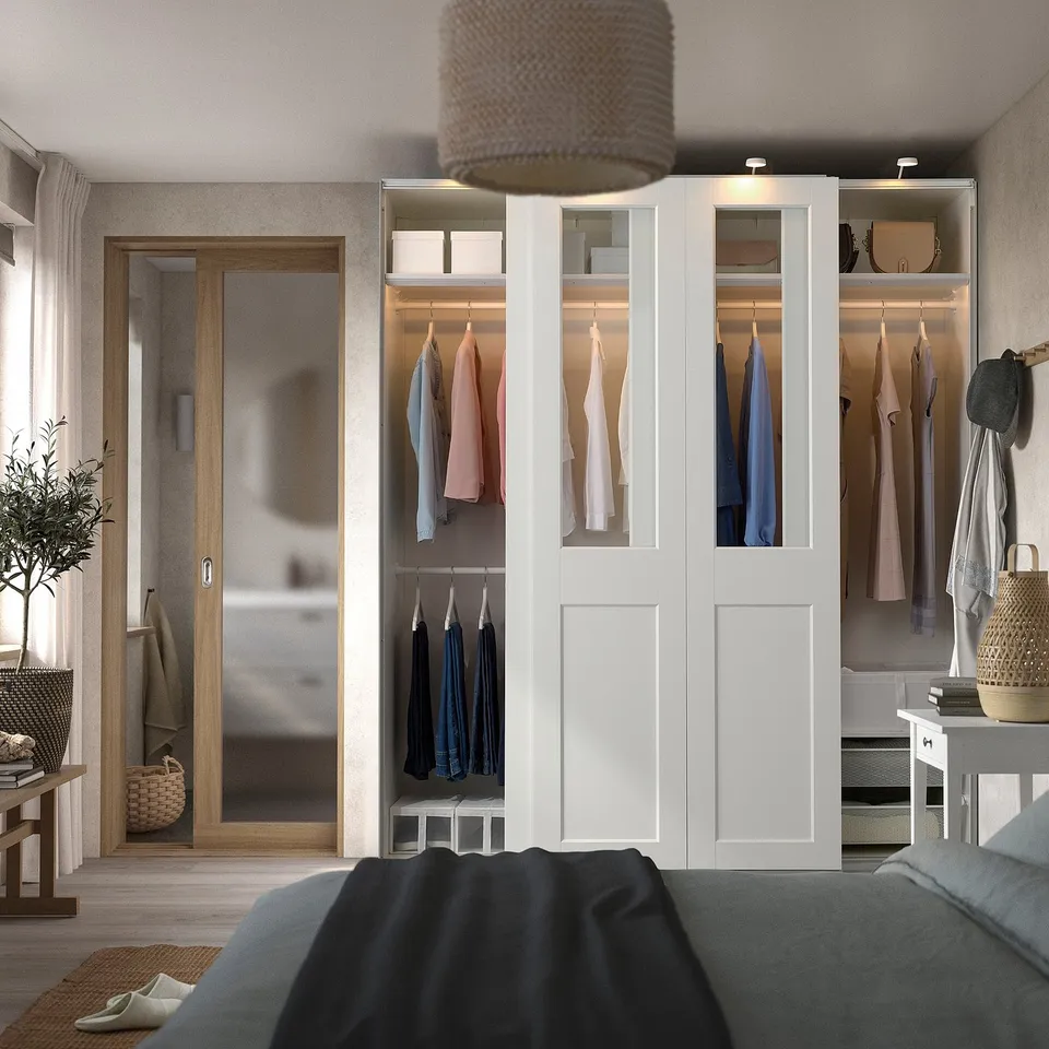 Modern bedroom with large white PAX wardrobe, sliding glass doors, integrated lighting, and storage.