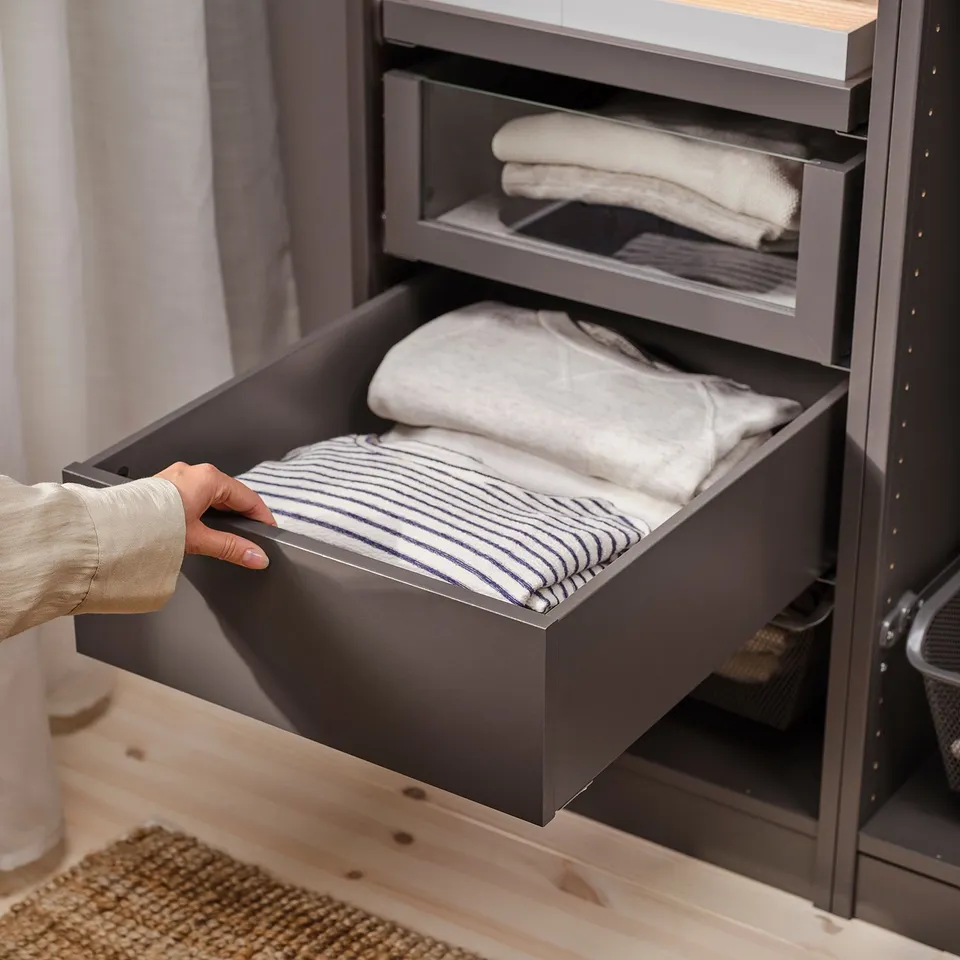 Grey KOMPLEMENT drawer, partially open, showing neatly folded clothes in modern design.