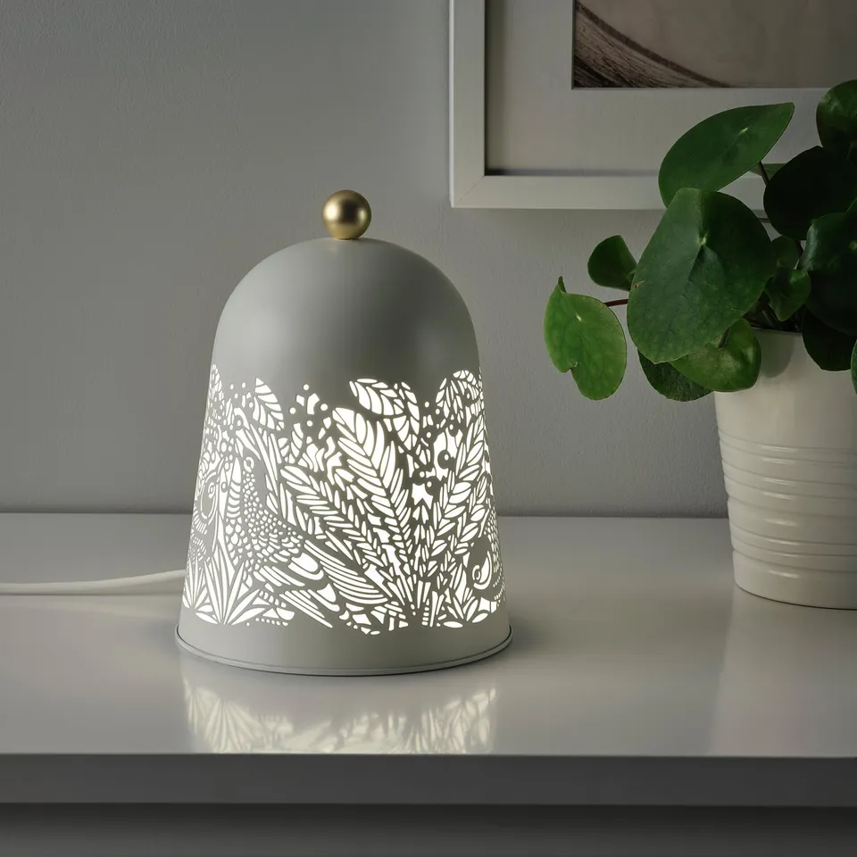 Grey table lamp with white leaf pattern, emitting soft light, placed on a white surface.