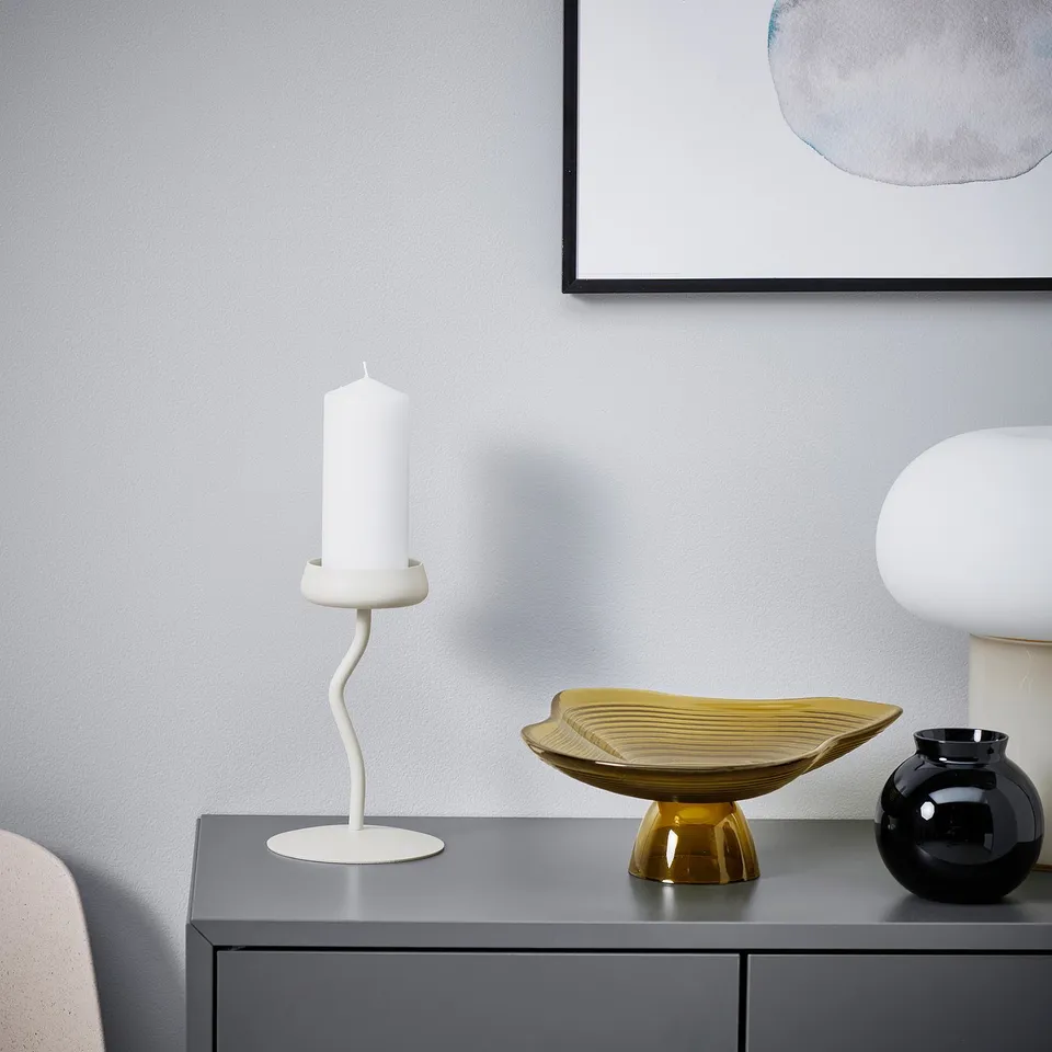 SILVERPÄRON white candlestick on dark console, slim & curvy, tall between black vase & golden bowl, modern art backdrop.