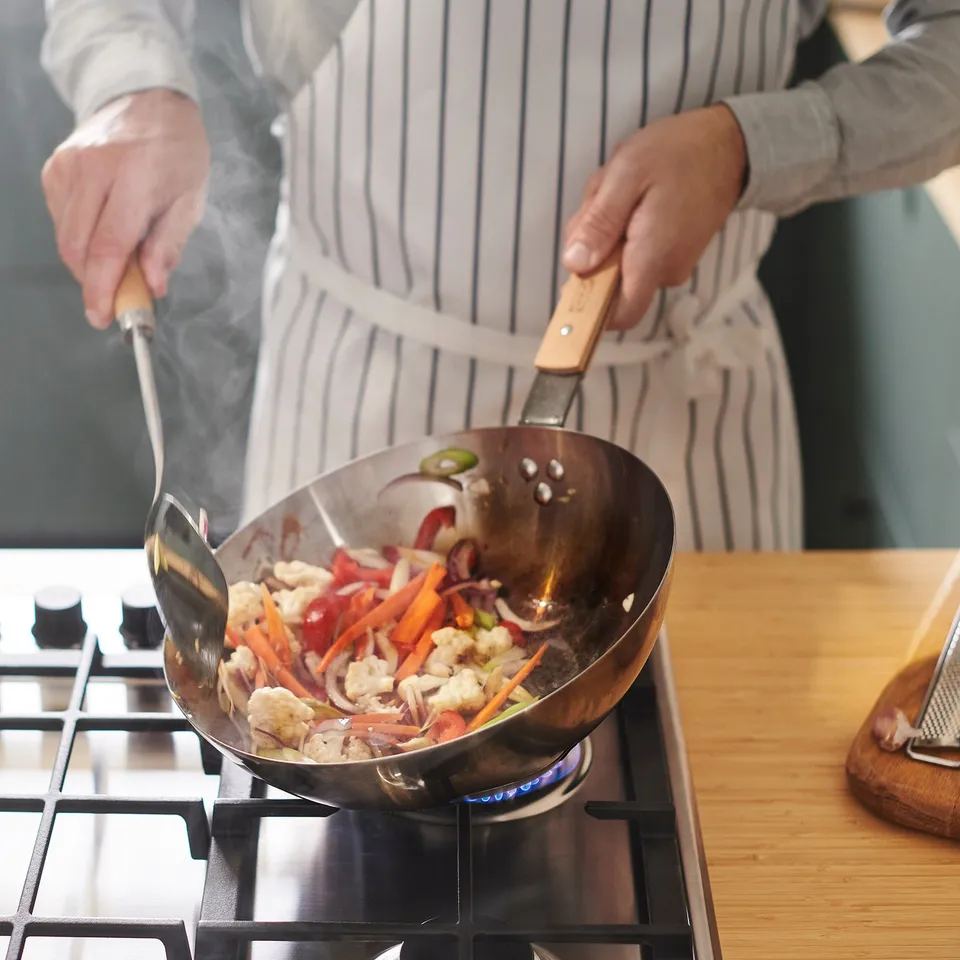 Person cooking vegetables in VARDAGEN wok with steam lid.