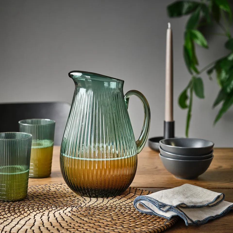 Glass jug with yellow beverage, glasses, bowls, candle, on table with placemat and napkin.