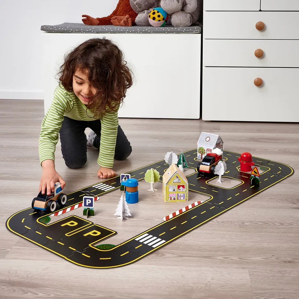 Child plays with toy car on detailed road set.