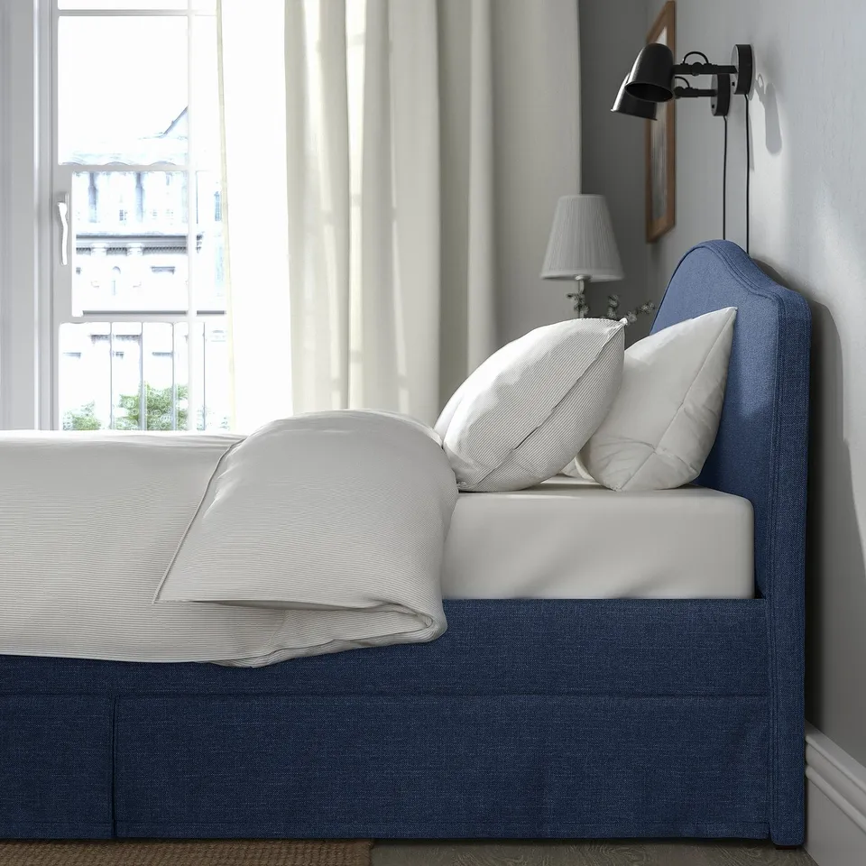 Bed with cushions, lamp, and window. Soft, upholstered headboard ideal for reading.