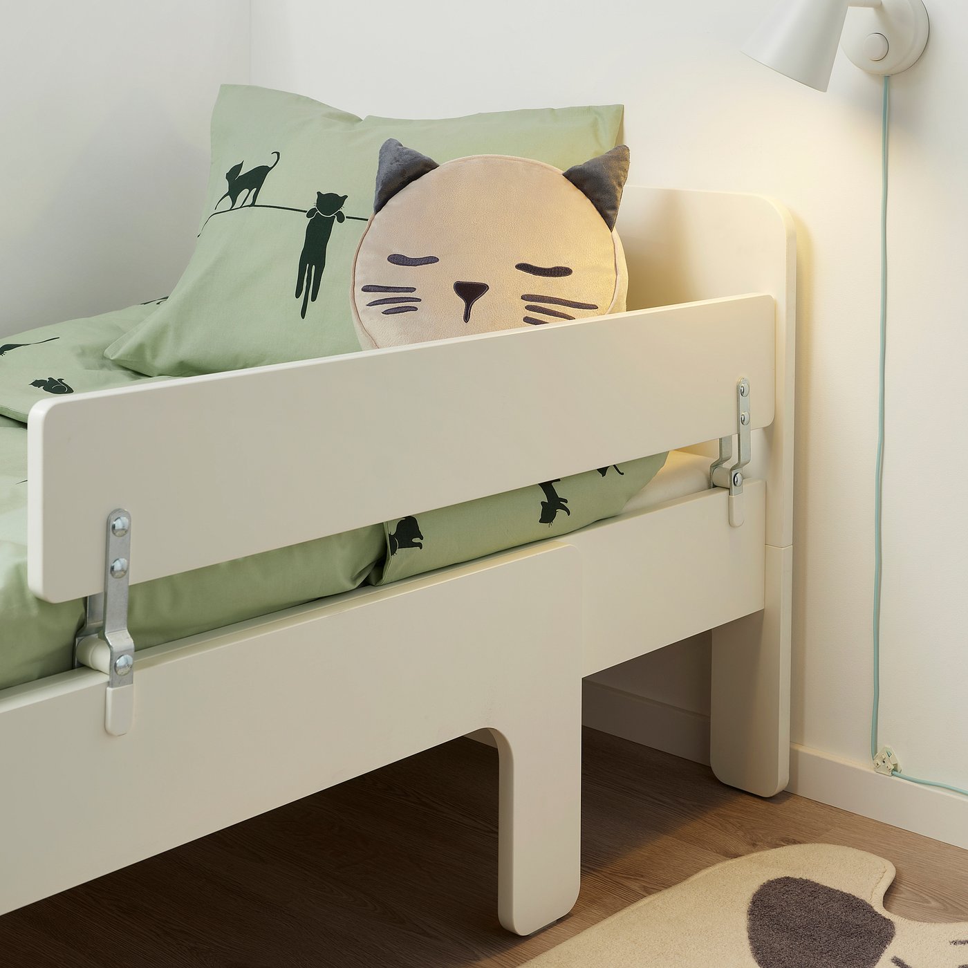 A childs bed with a white guardrail attached to prevent falls. The bed has decorative pillows with cat designs.