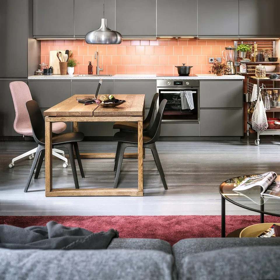 Modern kitchen with grey cabinets, pink tile backsplash, wooden dining table, and MITTLED pendant light.