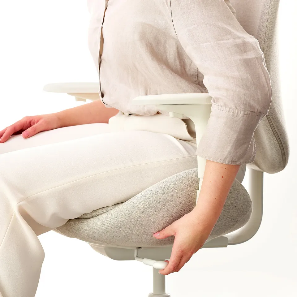Person sitting in ergonomic office chair, adjusting seat with armrests visible.