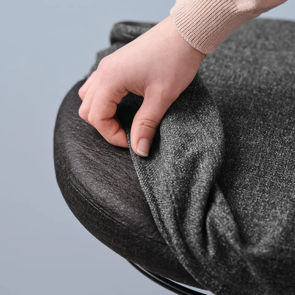 Person pressing on black circular stand support with grey fabric cover. Helps maintain active sitting for better posture.