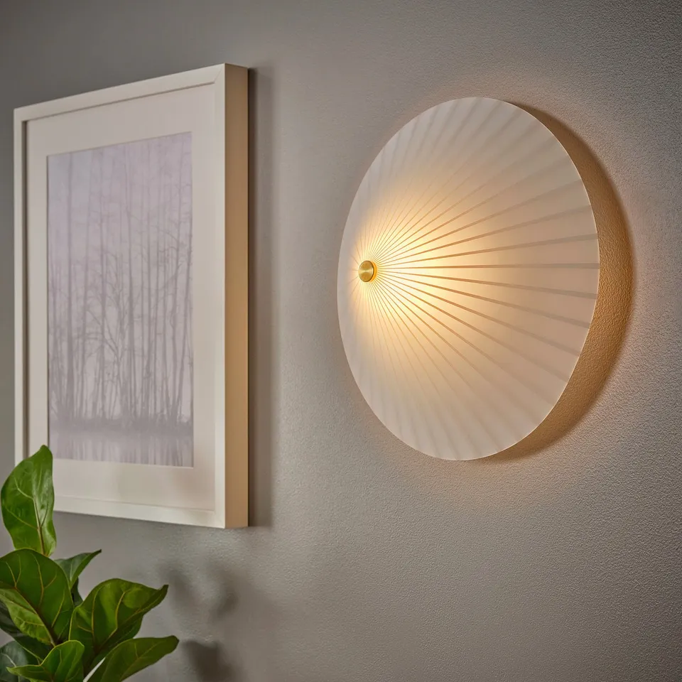 A modern, round wall lamp with an opal glass shade, mounted on a grey wall to the right of a framed photo, casting a soft light.