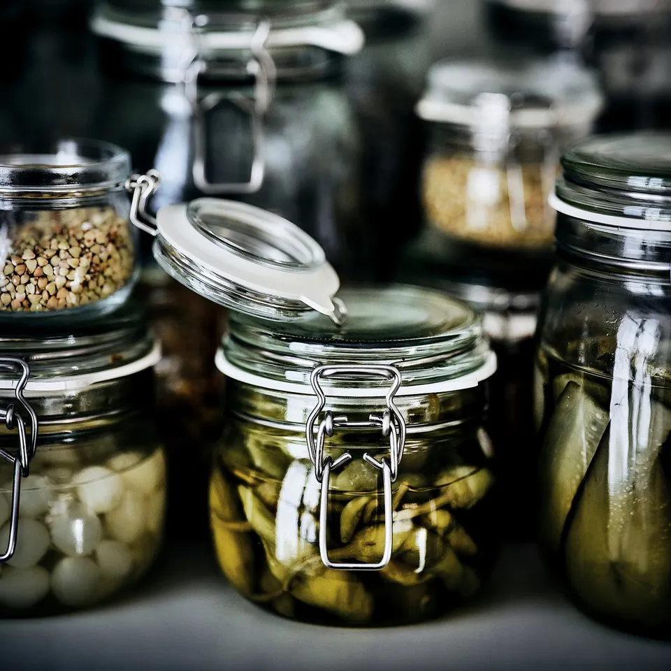 Glass jars with metal clips storing pickles and seeds, sealed for freshness.