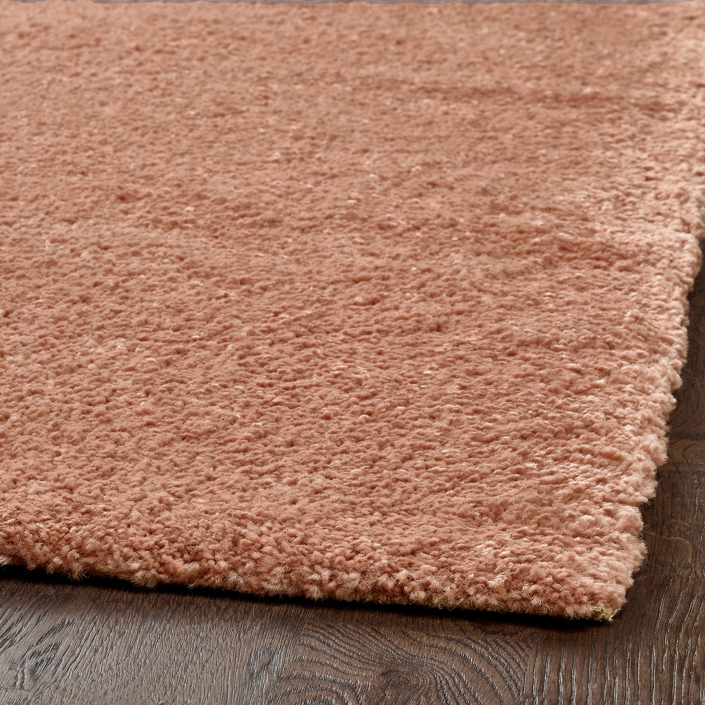 A close-up of a plush, pink area rug on a wooden floor. The texture is soft and dense, showcasing its high-quality material.