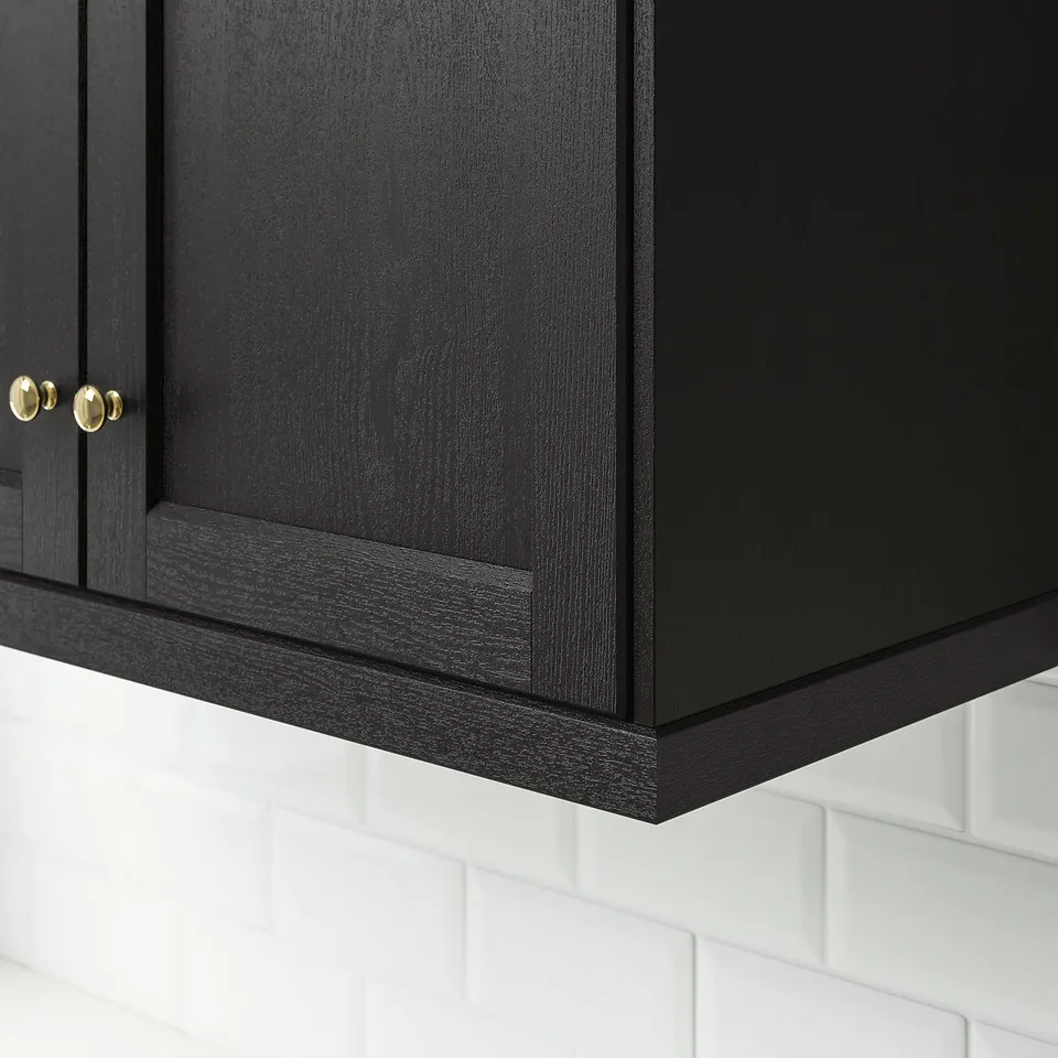 Black kitchen cabinet with gold knobs, mounted above white subway tiles.