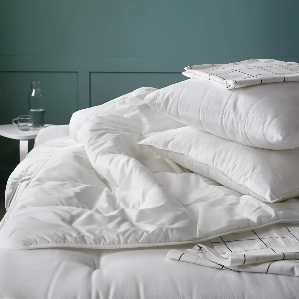 Bed with white SMÅSPORRE duvet, soft and fluffy. Light warm comfort, made with cotton and polyester. Duvet is folded neatly on a white bed.