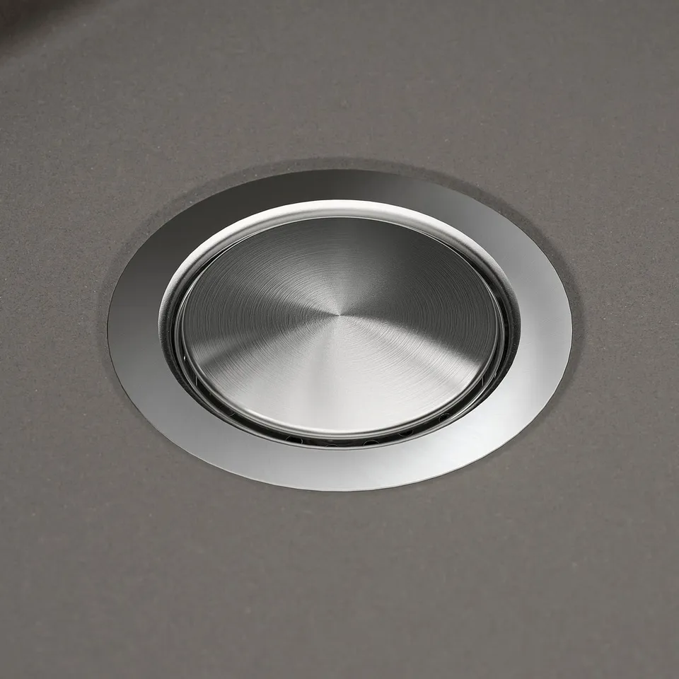 Stainless steel sink drain cover, integrated in sleek black quartz countertop. Polished, high-quality finish.