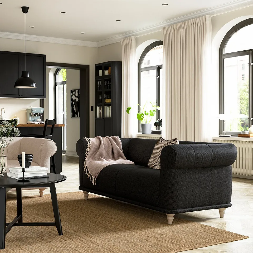 Modern living room with black VISKAFORS sofa, beige rug, arched windows, and black kitchen cabinets.