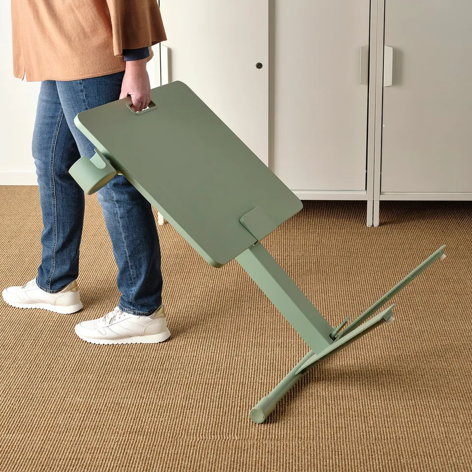 Person adjusting a green, height-adjustable laptop table in a room.