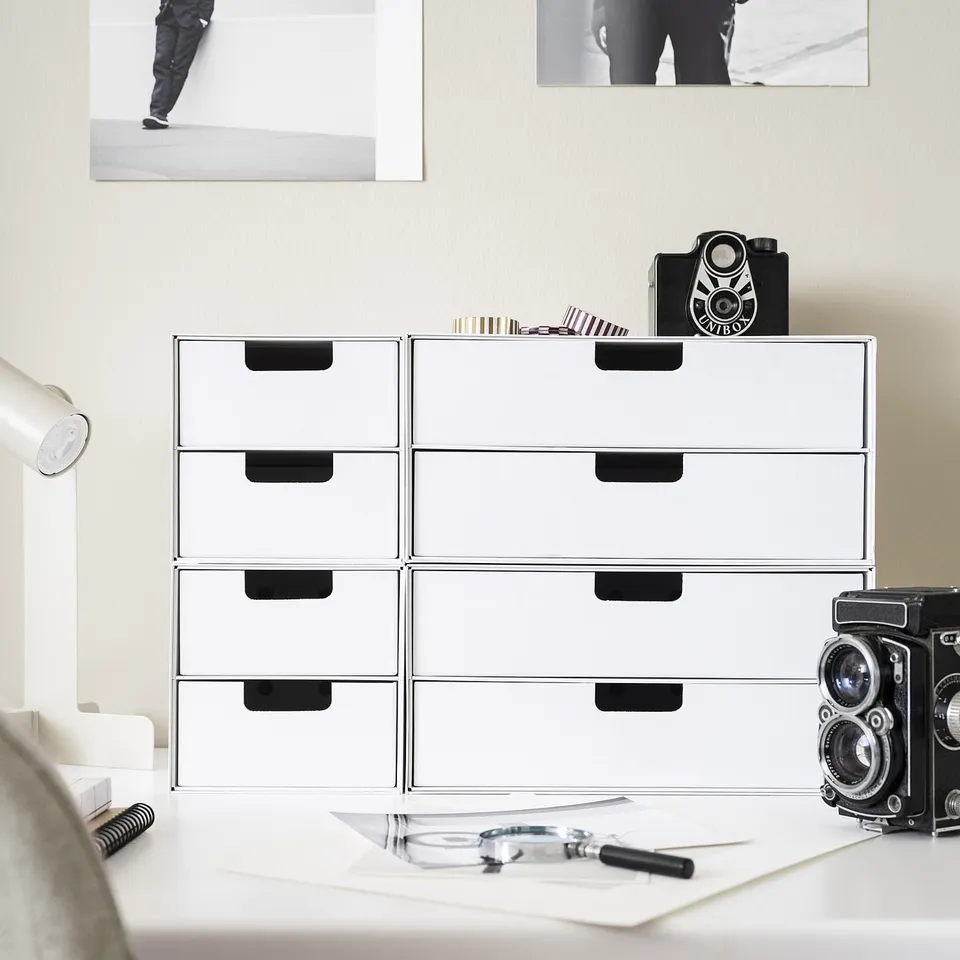 White FJÄDERHARV mini chest with black handles; made of recycled paper. Its small, stackable, fits in shelves and desks. On top sits a vintage camera.
