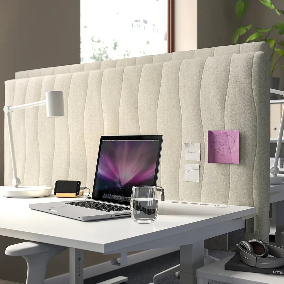 Modern white workspace with MITTZON acoustic screen. Laptop, glass, notes, lamp, headphones on wide desk. Screen tall, divides space, sound-absorbing.