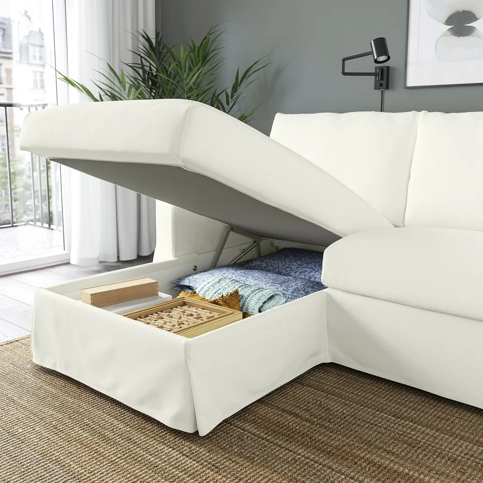 White sofa with open storage compartment revealing blankets and boards, showcasing hidden storage feature.
