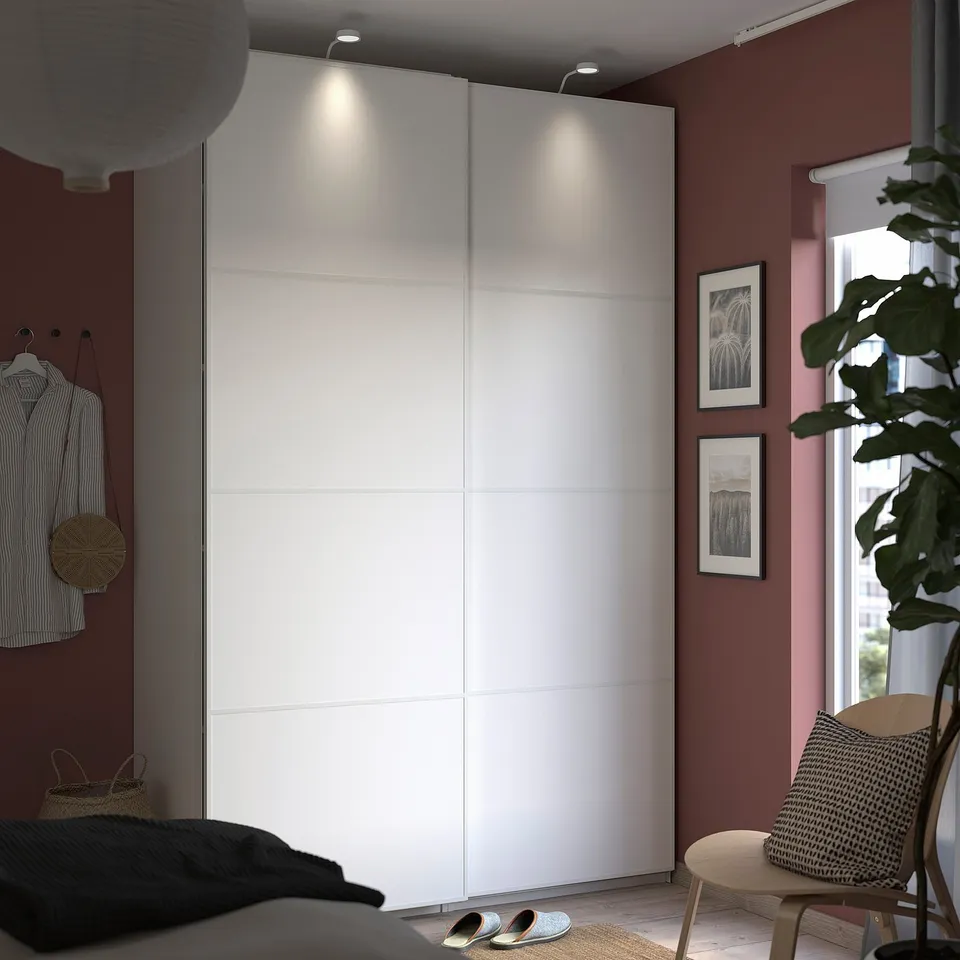 Modern bedroom with white PAX wardrobe, red wall, potted plant, striped shirt, slippers, wooden chair.