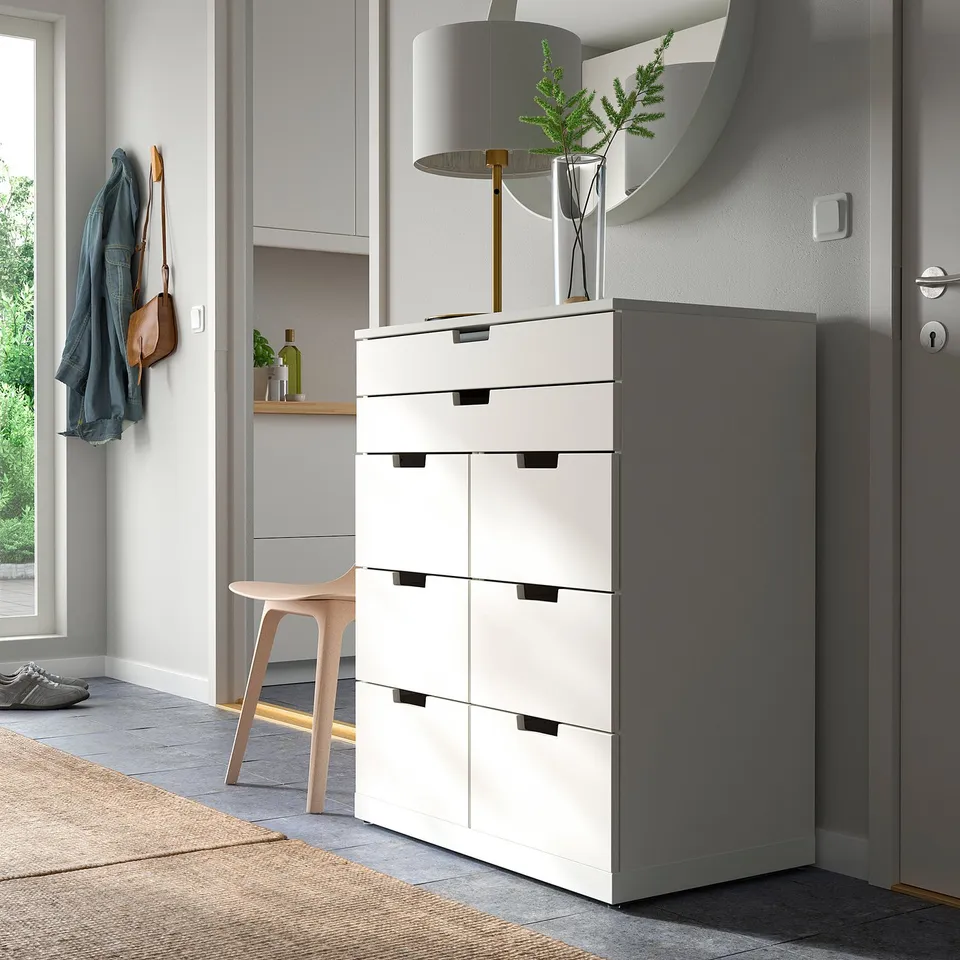 Modern white NORDLI chest of 6 drawers next to entrance, with lamp, mirror, and coat hook.