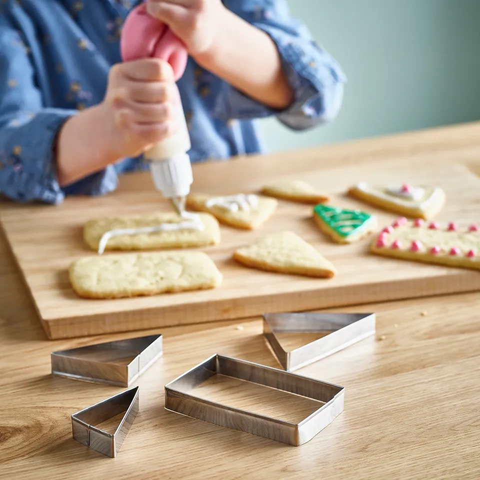 A child decorates cookies with icing on a wooden board using cookie cutters, showcasing baking creativity.