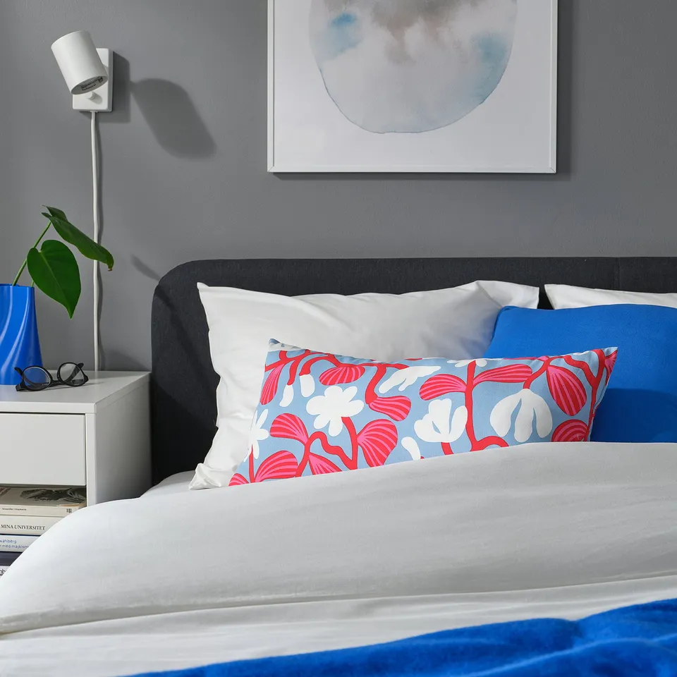 Brightly coloured SANDMOTT pillow on bed, large, light blue with red floral, cotton, rectangular.