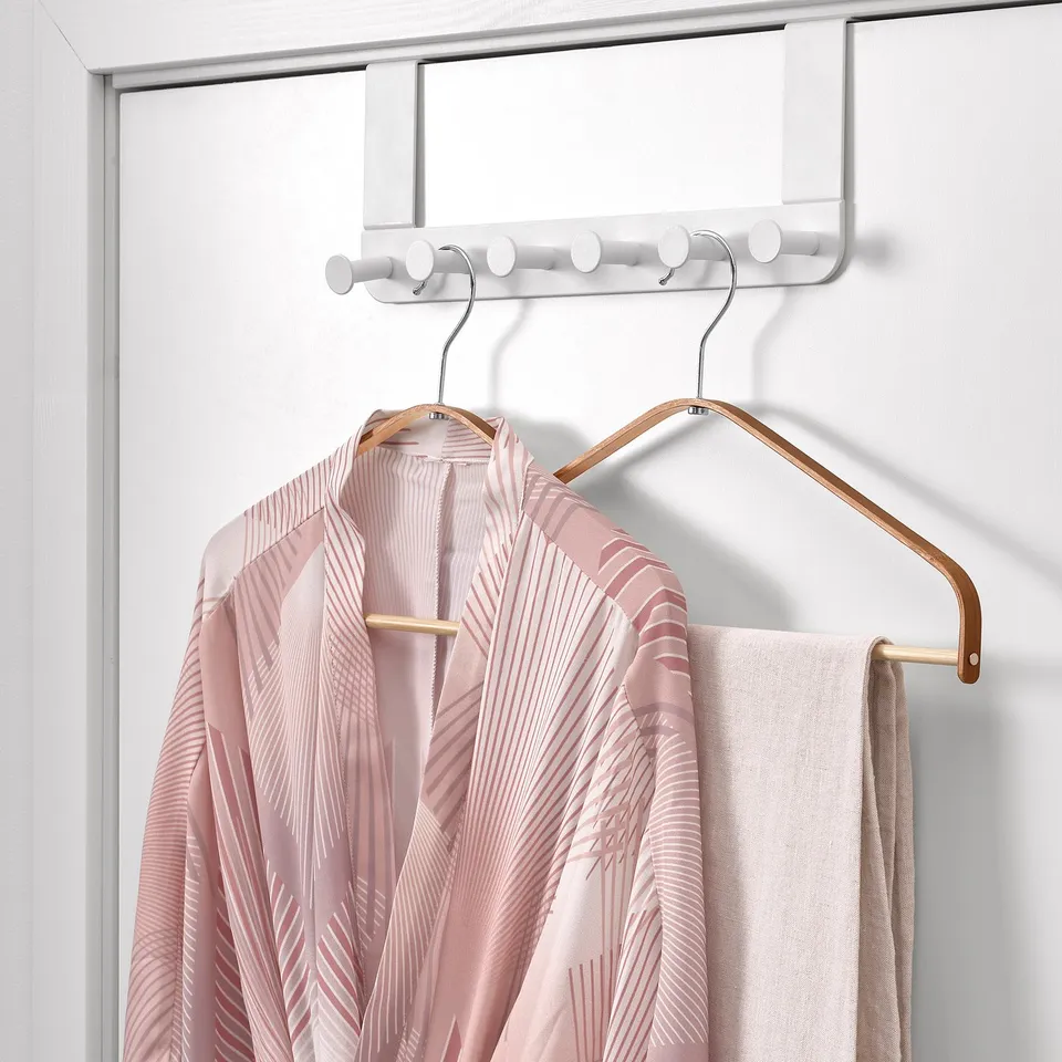 A light pink blouse with white stripes hangs on a bamboo hanger from a white rack with multiple hooks.