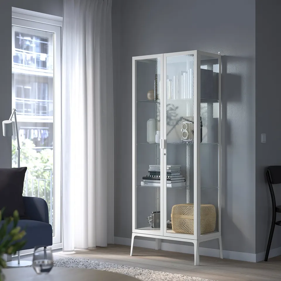 MILSBO cabinet with glass doors displays collectibles securely between window and chair.