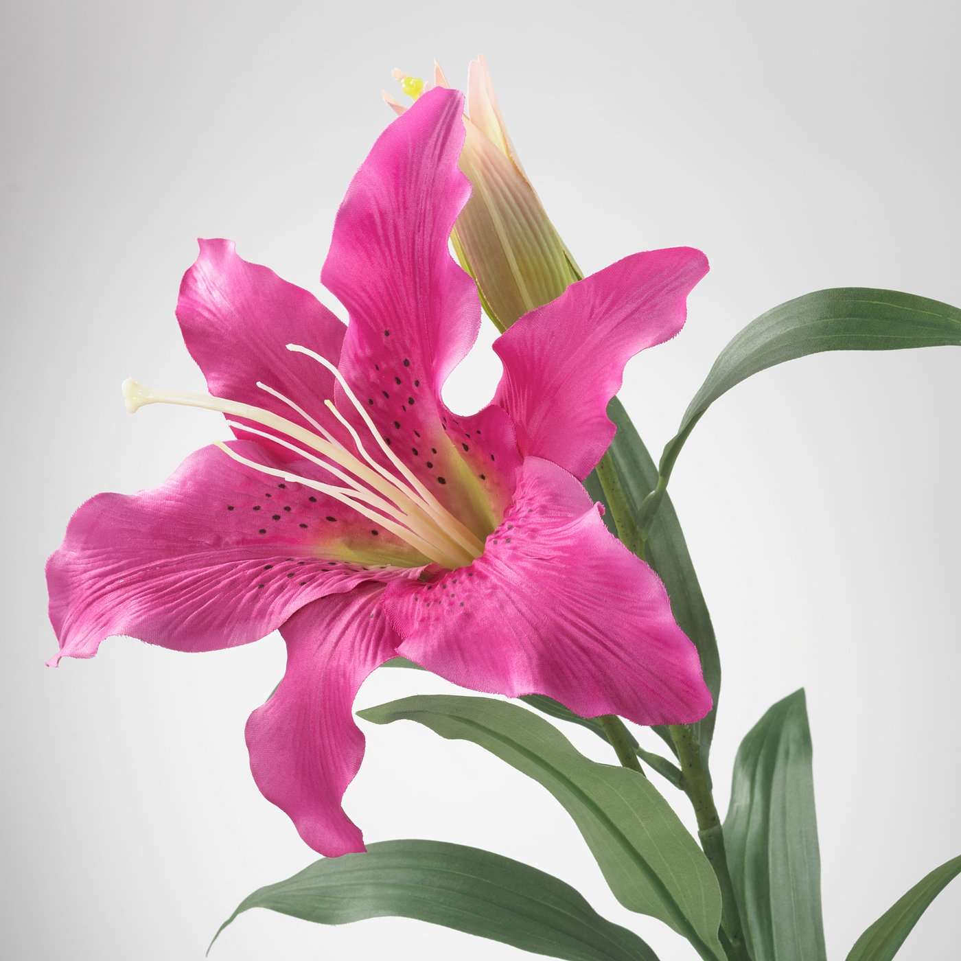 Vibrant artificial lily with vivid pink petals, yellow centre, green leaves.