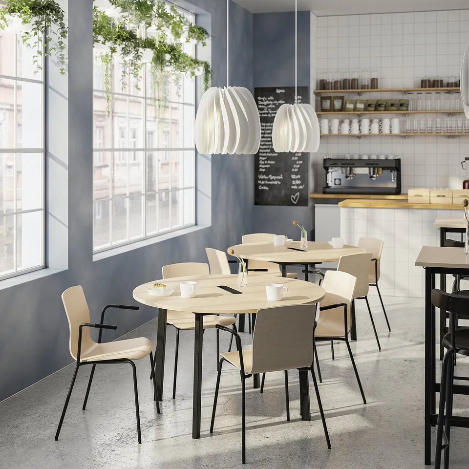 Modern cafe with mitzon round tables and läktare chairs, featuring light wood and minimalist design, set against large windows and greenery.