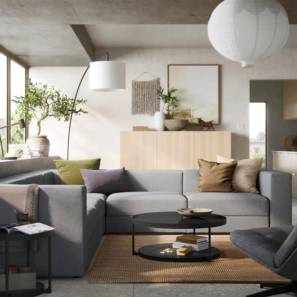 Modern living room with grey JÄTTEBO modular sofa, wooden console, potted plant, pendant lights, and colourful cushions.