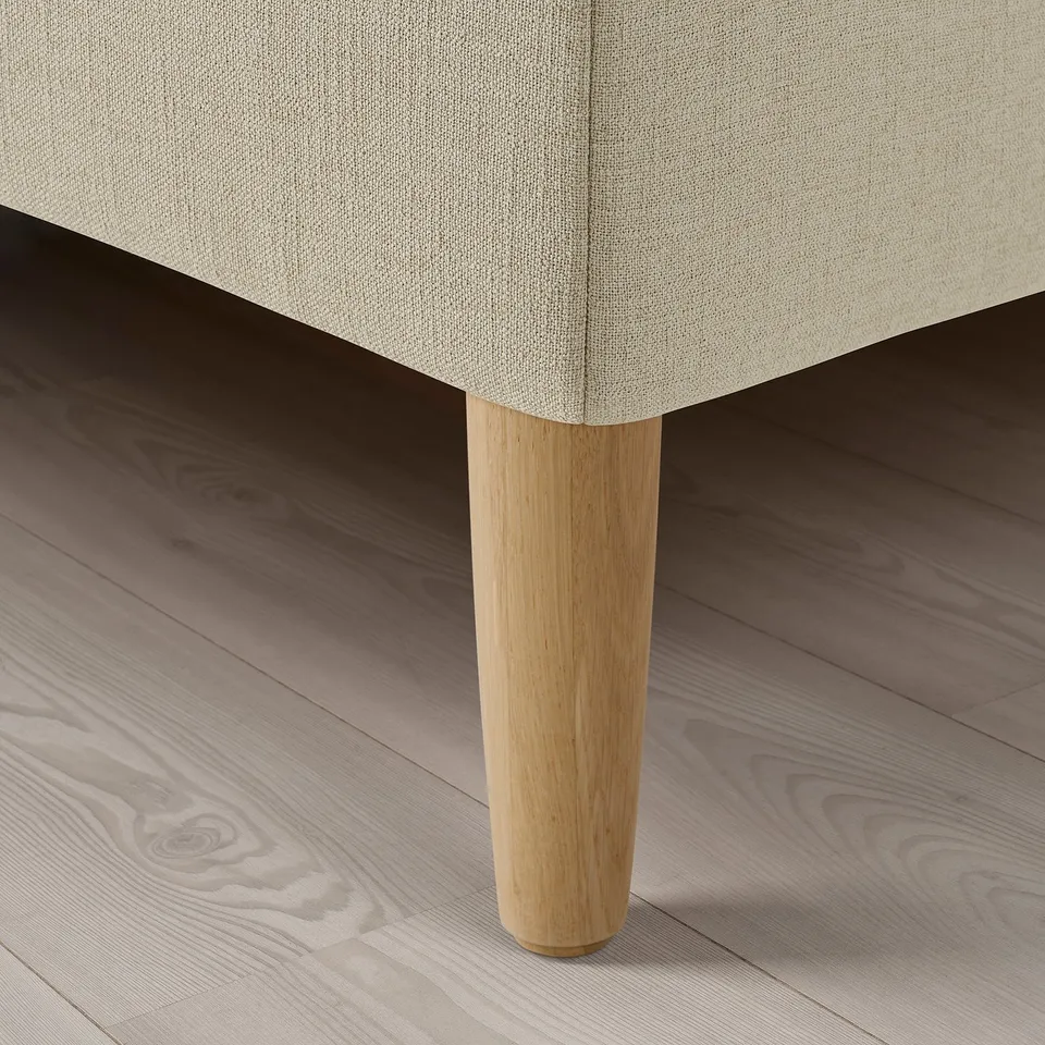 Close-up of upholstered bed corner, showcasing soft beige fabric and sturdy wooden leg.