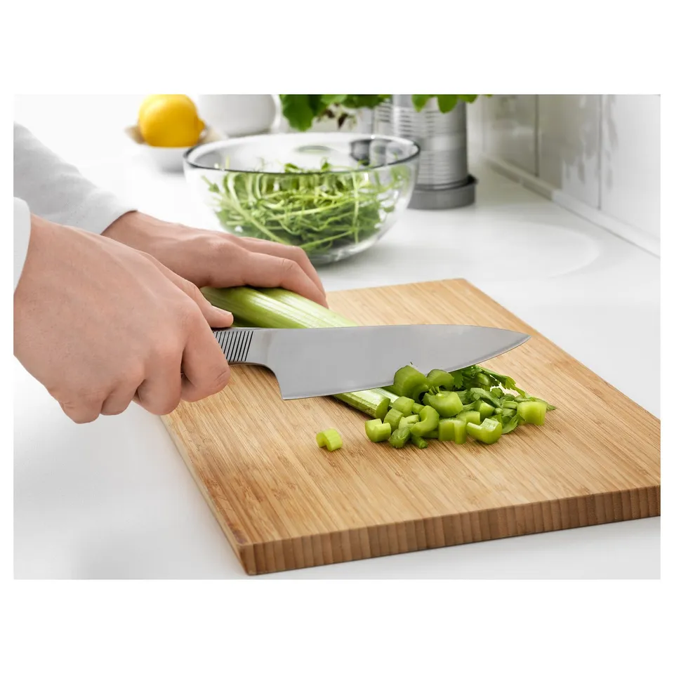 A person is chopping celery on a wooden cutting board using a stainless steel knife. The knife has grooves on the handle for grip.