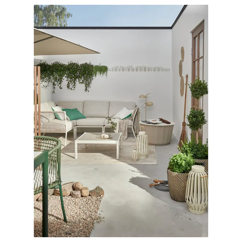 Modern outdoor patio with white sofa, wicker chairs, glass table, plants, and decor.