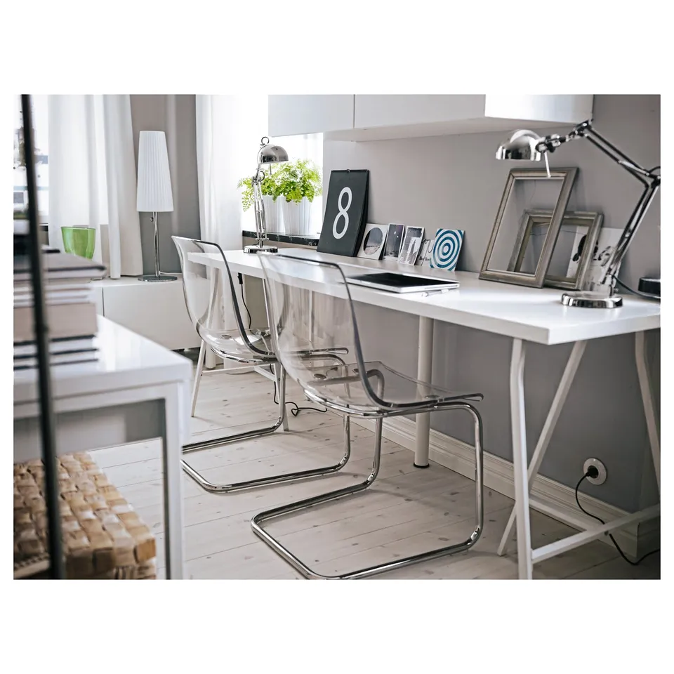 Modern office setup with white and clear-chair desks, featuring a silver task lamp and decorative items.