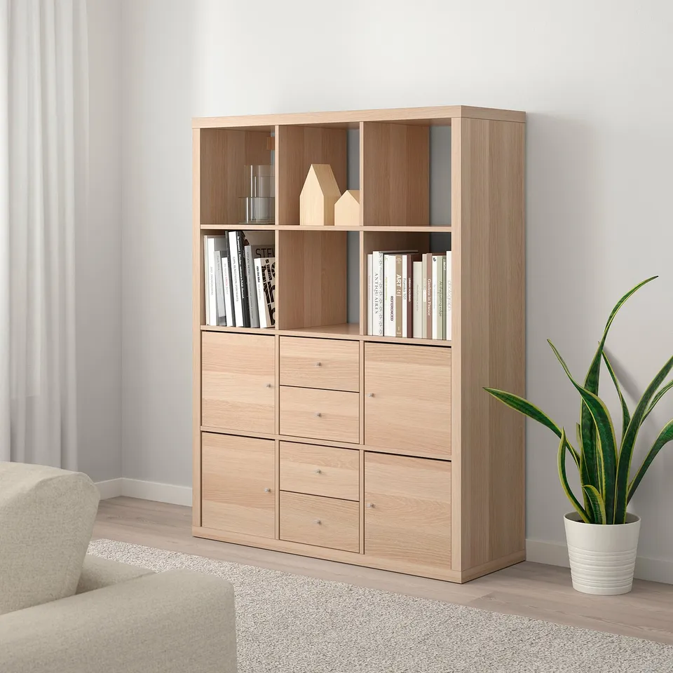 KALLAX shelf with drawers, books, and decor. Armchair left, plant right.